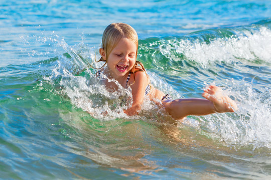 Happy family lifestyle. Baby girl splashing and jumping with fun in breaking waves. Summer travel, water sport outdoor activities, swimming lessons on tropical beach holiday with kids.