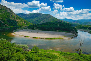 Fototapeta premium Valley of Arda river near Madzarovo, Bulgaria, Eastern Rhodopes. Summer day in Bulgaria. River Landscape with green hills. Traveling Balkan, Europe. Water, blue sky, white clouds. Mountains, Europe