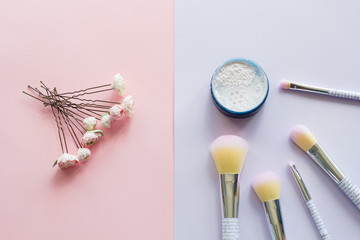 Five makeup brushes with lettering on the handle and mineral powder in a blue jar, wedding hairpins for hair with handmade peonies made of plastic on pink and purple background. Have copy space.