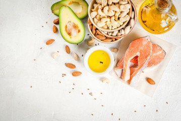 Healthy food. Products with healthy fats. Omega 3, omega 6. Ingredients and products: trout (salmon), flaxseed oil, avocado, almonds, cashews, pistachios. On a white stone table. Copy space top view - obrazy, fototapety, plakaty
