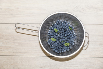 Blueberries and mint leaves in colander on wooden background