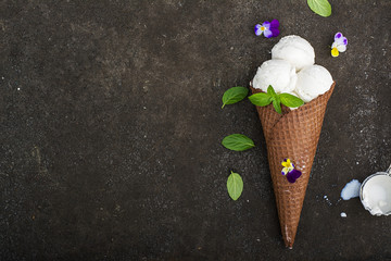 Balls of creamy vanilla ice cream in a crispy chocolate mug with edible viola flowers and mint...