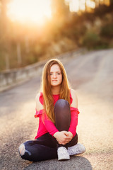 Teenager sitting on the empty road in sunset lights