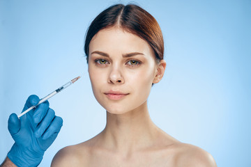 Young beautiful woman on a blue background holds a syringe, medicine, plastic surgery
