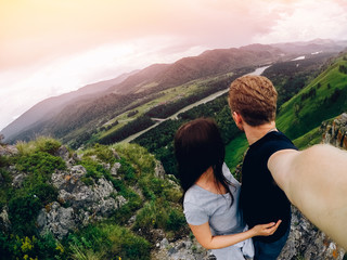 Fototapeta na wymiar Guy and girl tourists are happy, hug and do selfie on action camera on background of mountains, forests. Concept love and travel. Russia, Altai Mountains.