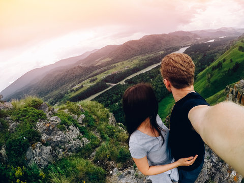 Guy and girl tourists are happy, hug and do selfie on action camera on background of mountains, forests. Concept love and travel. Russia, Altai Mountains.