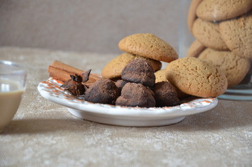 Chocolate truffles of candy on a plate, with cinnamon and anise. On a serviced table, cup of cofee, cookie
