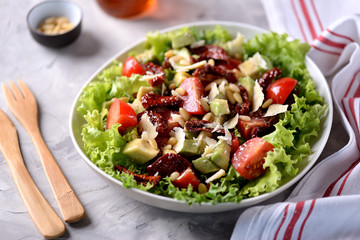 Salad from lettuce, cherry tomatoes, dried tomatoes, avocado, parmesan, pine nuts with olive oil. Healthy food.
