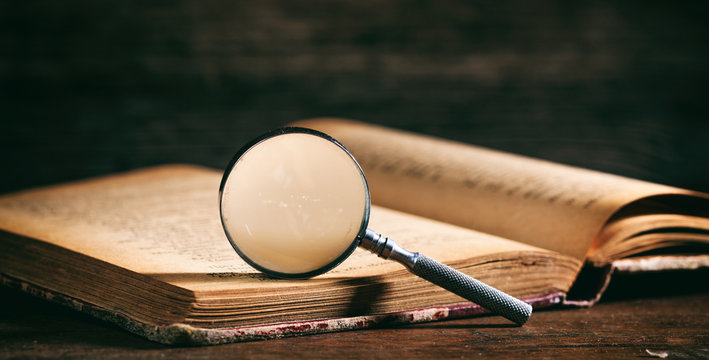 Vintage book and magnifying glass on wooden desk