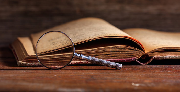 Vintage book and magnifying glass on wooden desk