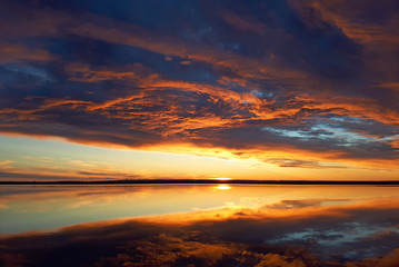 Cumulus sunset clouds with sun setting down. Fiery orange sunset sky. Beautiful sky.