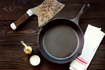 Cast-iron frying pan with salt and pepper on a wooden background.