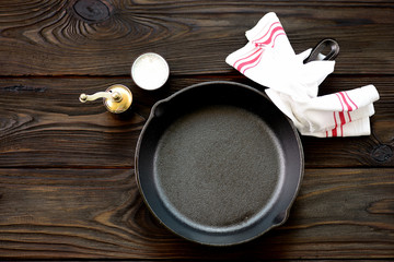 Cast-iron frying pan with salt and pepper on a wooden background.