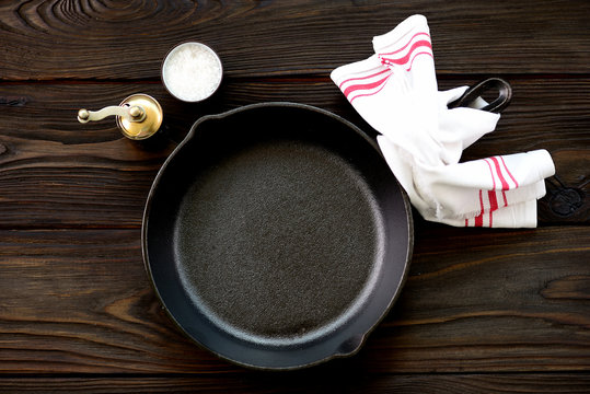Cast-iron frying pan with salt and pepper on a wooden background.
