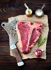 Raw t-bone steak with garlic and rosemary on an old wooden background. Rustic style.