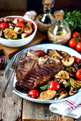 Grilled t-bone steak with grilled vegetables on an old wooden background. Rustic style.