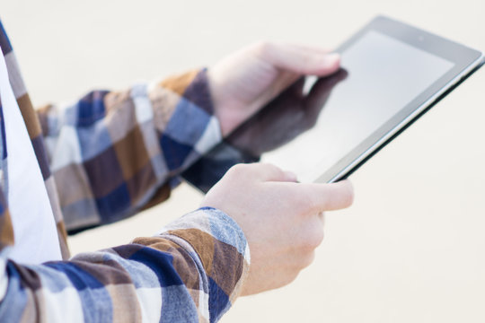 Close-up: man in a hipster style with tablet in hands combining work with relax on the beach of Baltic Sea