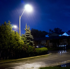 Rain pouring down on stormy night, residential street with water lit by lamp post