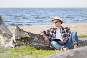 A man in smart casual hipster style with tablet combining work with relax on the beach of Baltic Sea