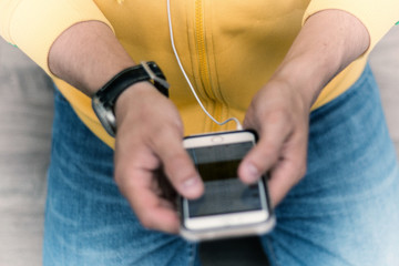 Close up of man's hands browsing phone with headphone jack plugged in