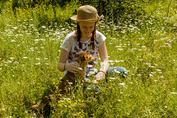 Smiling young girl with hair braids and hat with her pet dog in a field