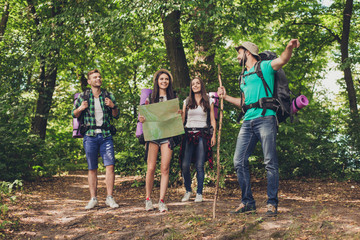 Camping, trekking, wild life concept. Four best friends are hiking in the spring woods, the guy is showing the direction, lady is checking it on a map, all are excited and anxious