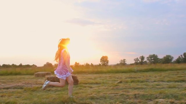 Happy little girl in a field with hay rolls at sunset