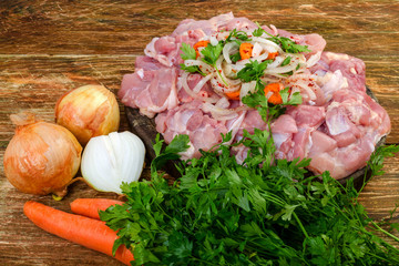 Fresh raw chicken meat and onion, carrot, spices and greens  prepared for cooking,  on the wooden background.