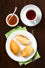 Toasted bread rolls with peach jam in bowl and tea on the side, photographed overhead on dark wood with natural light
