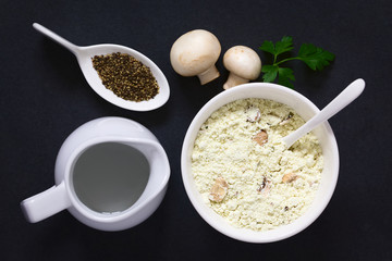 Instant mushroom soup powder in bowl with water and black pepper on the side, photographed overhead on slate with natural light (Selective Focus, Focus on the soup powder)