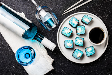 Blue sushi rolls and blue wine chardonnay on black background. Spanish blue wine, trendy drink, Fancy wine, top view. Copy space