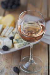 A glass of rose wine served with cheese plate, blackberries and baguette
