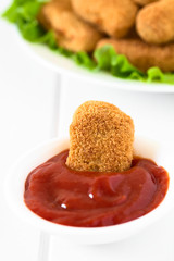 Fried breaded crispy chicken nugget dipped in ketchup, photographed with natural light (Selective Focus, Focus on the front of the chicken nugget in the ketchup)