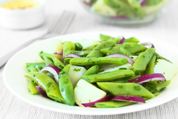 Green bean, potato and red onion salad with parsley, hollandaise sauce in the back, photographed with natural light (Selective Focus, Focus in the middle of the salad)