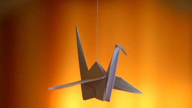 Delicate origami bird spinning by thread on yellow background, imagination
