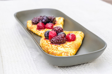 Crepes with wild berries on a grey plate on a white towel.