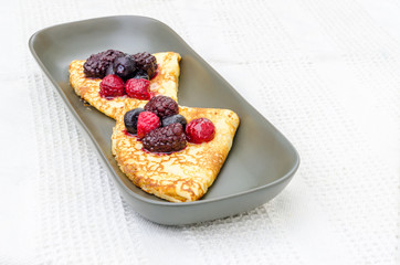 Crepes with wild berries on a grey plate on a white towel.