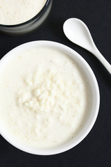 Kefir grains in milk with a glass of fresh kefir drink on the side, photographed overhead on slate with natural light (Selective Focus, Focus on the top of the kefir grains and the kefir drink)