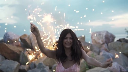 Portrait of a cheerful girl on the background of fireworks. Attractive girl having fun and dancing at a party holding bengal lights. slow motion