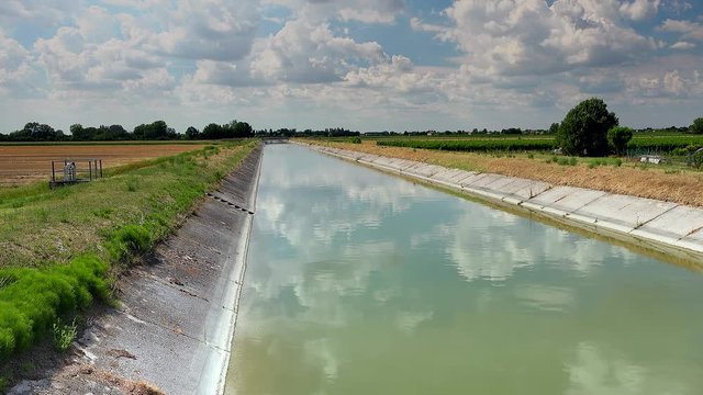 Engineering built this artificial canal to bring water to cultivated fields, here flowing peaceful under a summer blue sky of white clouds, color graded clip