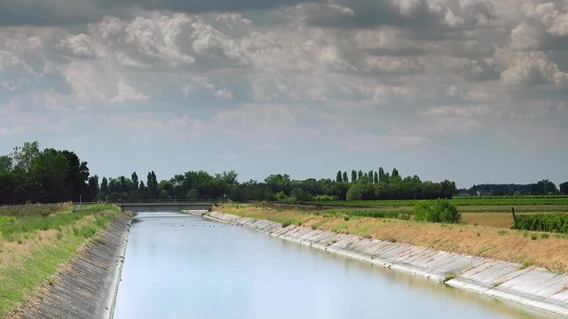 timelapse shot of artificial canal bringing water to cultivated fields, here flowing peaceful under a summer blue sky of white clouds, color graded clip