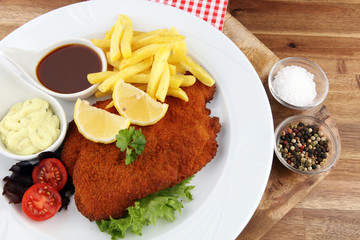 Dish of Wiener schnitzel and French fries served with sauces and salad on rustic wooden table