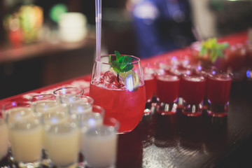 Line of different colored alcohol cocktails on a decorated catering banquet table on a party