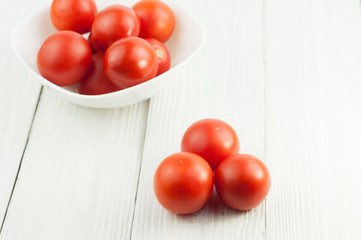 Three alone and many ripe tomatoes in bowl on old white wooden planks