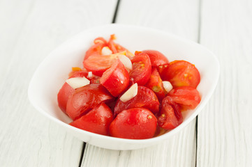 Salad with ripe fresh red tomatoes in bowl on white wooden planks