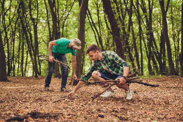 Close up photo of two guys friends in the wood in fall, collecting wood for a camp fire, nice view of a forest in the autumn