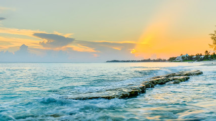 Obraz premium Sunset over a flat rock sticking out of the Caribbean sea at Cemetery Beach, Grand Cayman, Cayman Islands