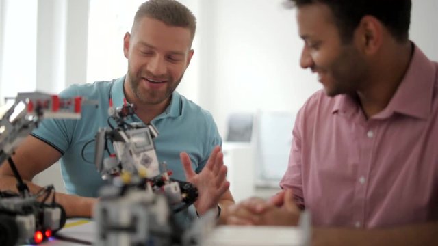Radiant male colleagues discussing advantages of robotic devise