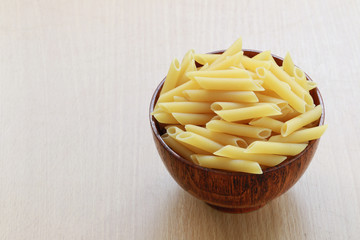 Raw Macaroni in the wooden bowl on wood background.