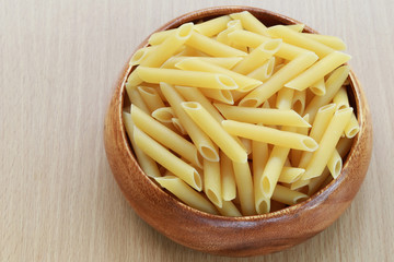 Raw Macaroni in the wooden bowl on wood background.